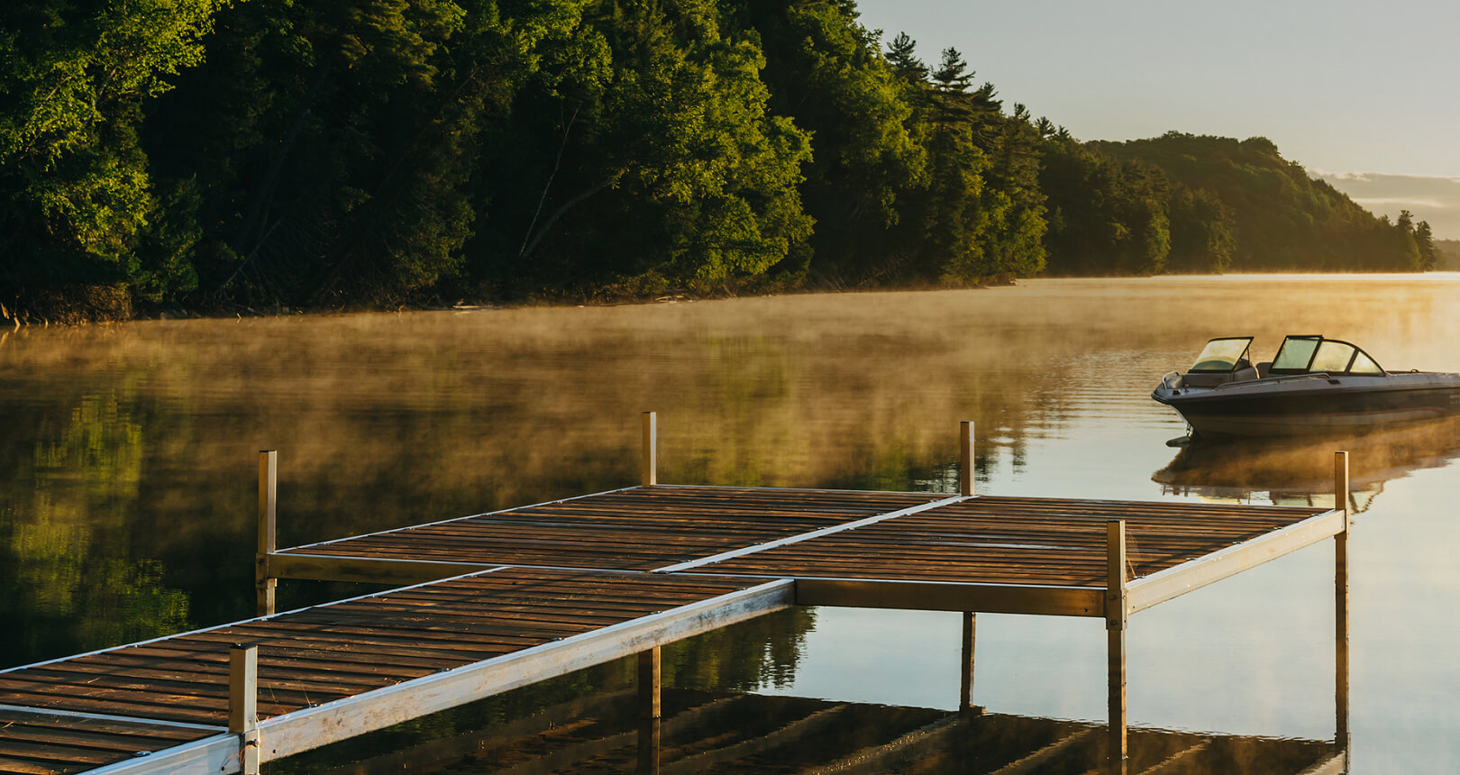 A boat and dock on a peaceful, still lake in the early morning hours.